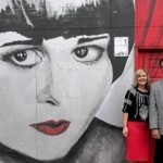 Three people standing in front of a mural of a woman with popcorn.