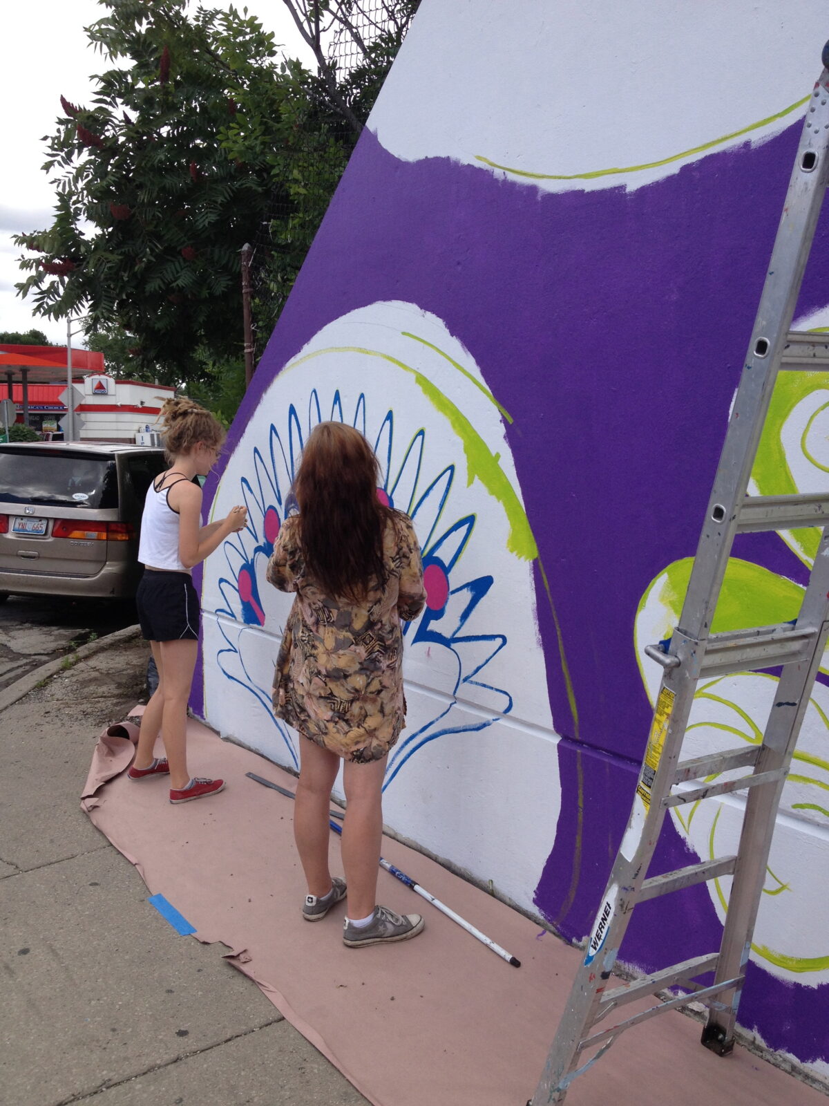 Two women painting a mural on a wall.