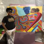 Artist standing beside colorful abstract painting.