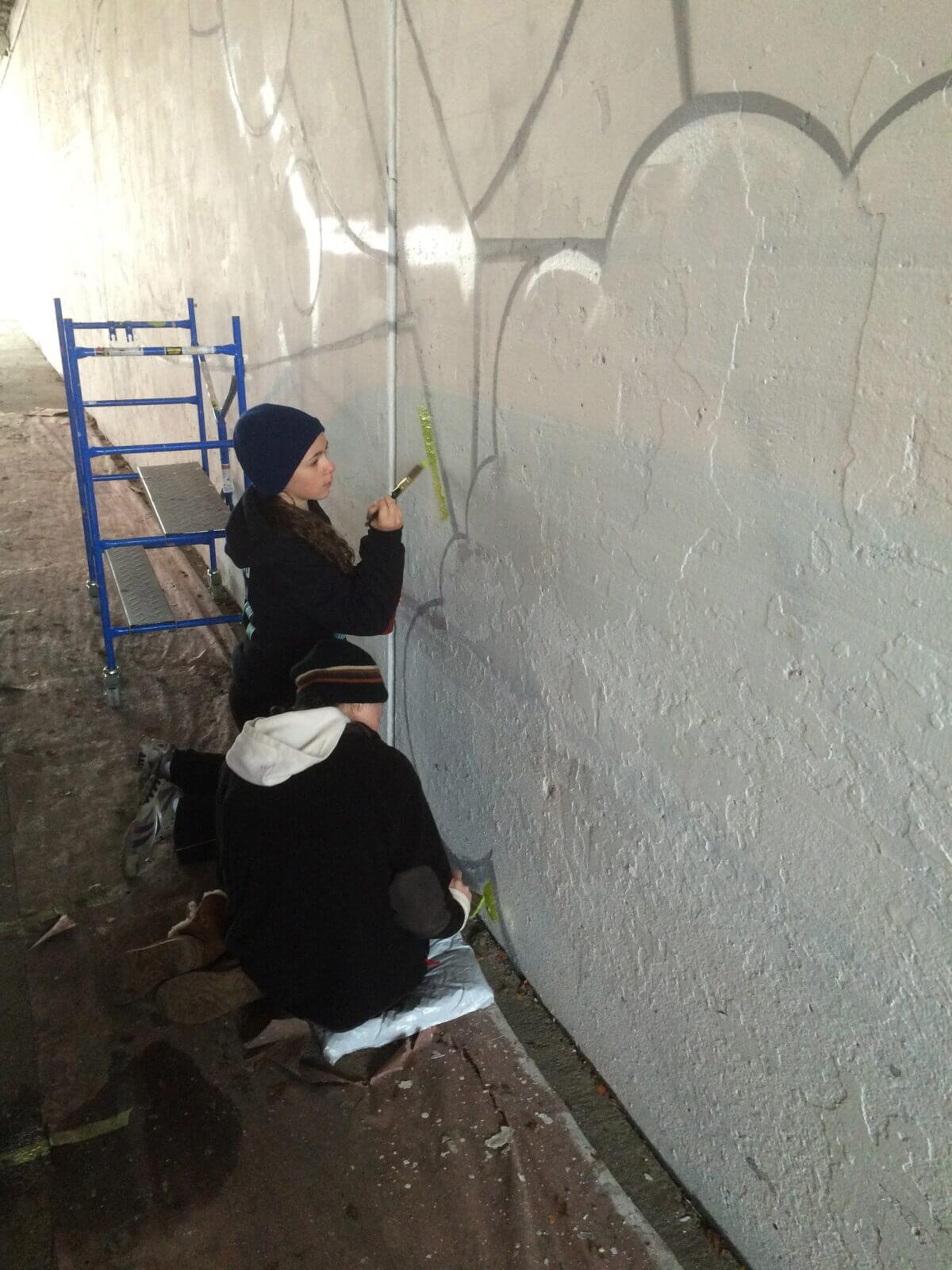 Two people painting graffiti on a wall.