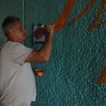 A man is painting on a blue wall.