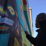 A man painting a colorful mural on the side of a building.