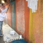 Man painting a colorful wall white.