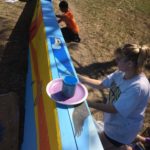 A group of people painting a long piece of wood.