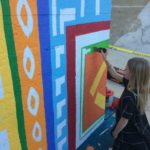 A young girl painting a colorful wall.