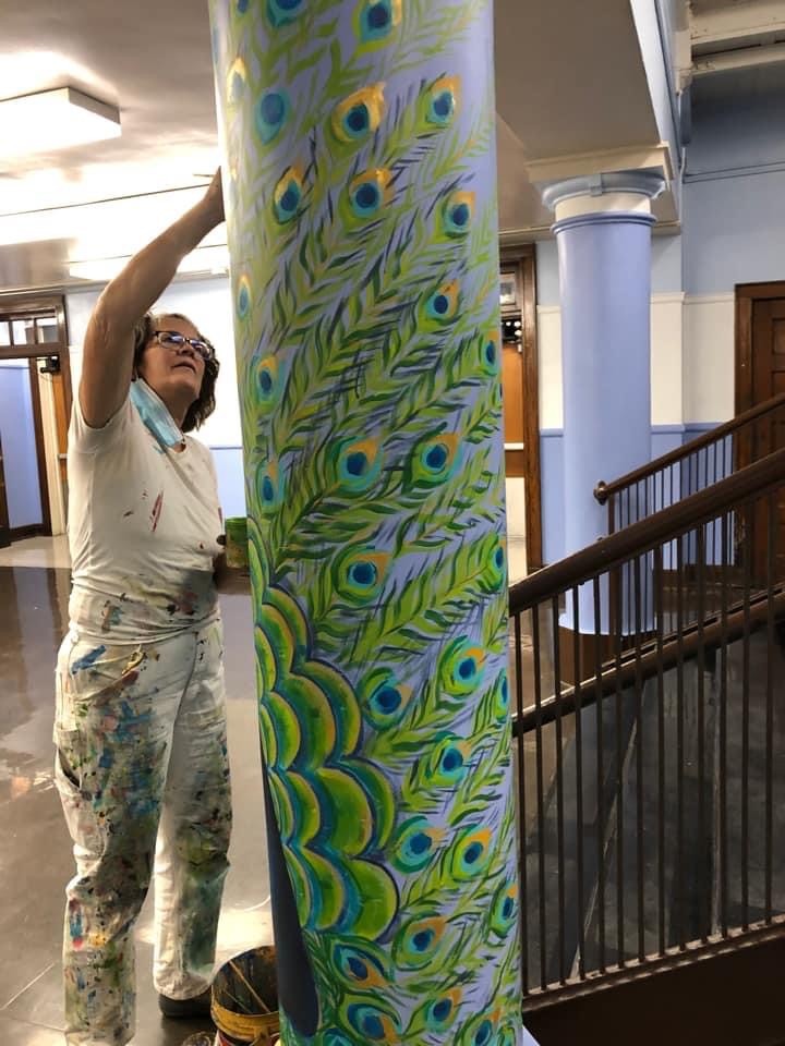 Artist painting colorful peacock feathers on column.