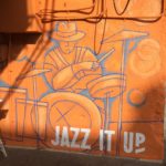 A mural of a man playing drums on an orange wall.