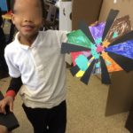 A young boy holding up a colorful paper flower.