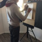 A man drawing on an easel in a room.