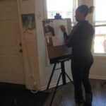 A woman painting on an easel in front of a door.