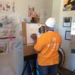 A woman in an orange shirt drawing on an easel.