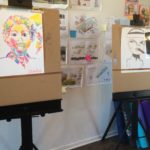 Two easels with drawings on them.