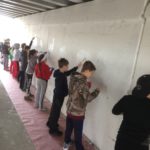 A group of kids painting a wall under an overpass.