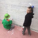 Two boys playing with paint on a wall.