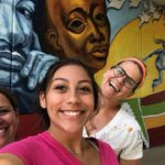 Three women taking a selfie in front of a mural.