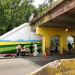 A group of people painting a mural under an overpass.