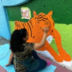 A woman paints a tiger on a wall.