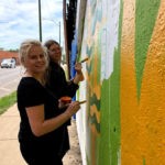 Two women painting a mural on a wall.