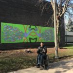 Person in wheelchair near colorful wall mural.
