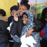 Two girls hugging each other in front of a group of people.