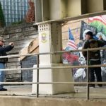 A police officer takes a picture of a mural on the side of a bridge.