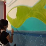 A girl painting a fish on a wall.