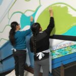 Two people painting colorful mural on wall.