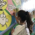 Girl painting colorful animal mural on wall.