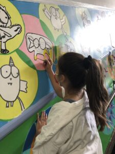 Girl painting colorful animal mural on wall.