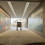 A pedestrian walkway with vibrant murals on both sides leading to an urban street.