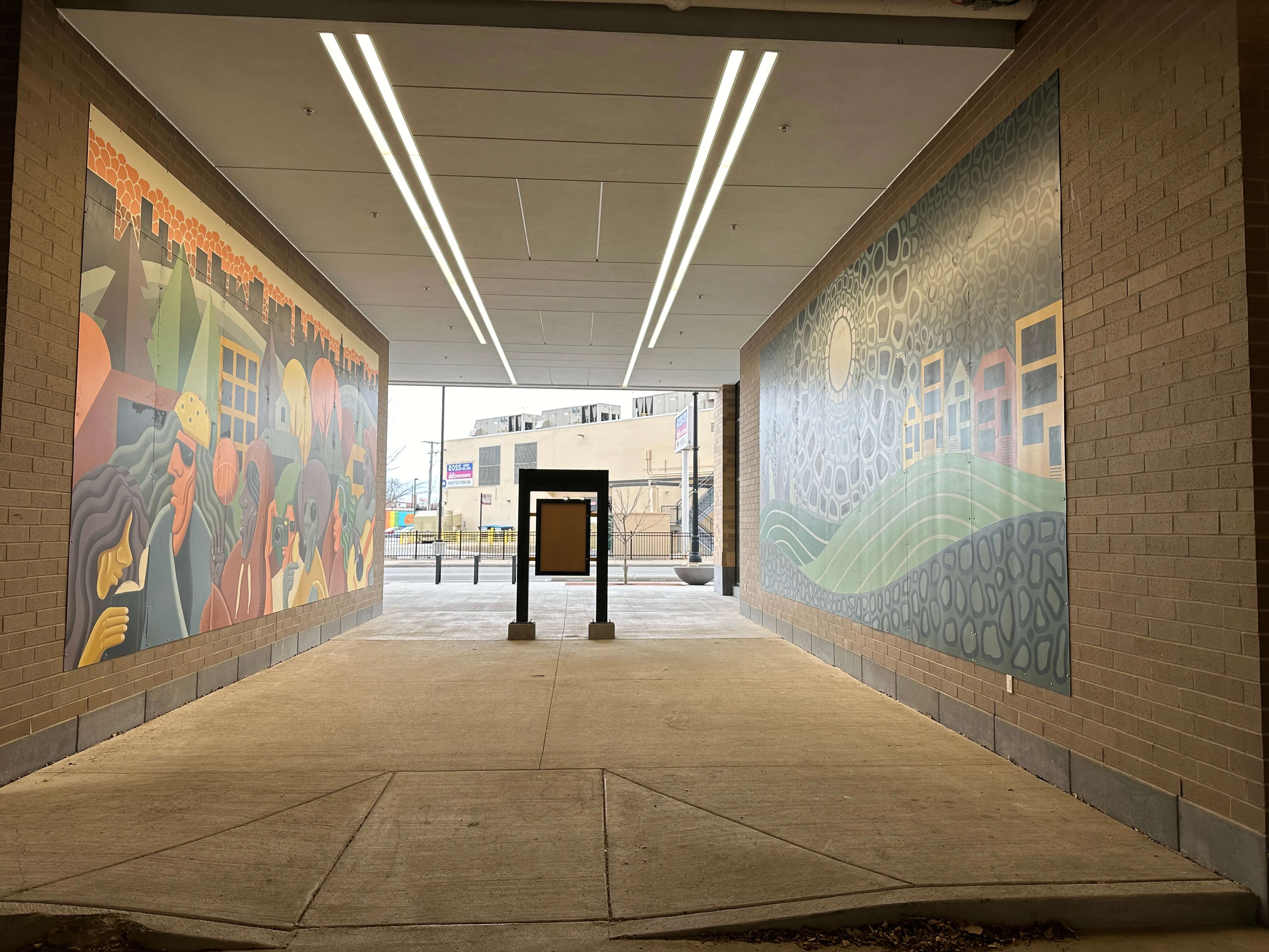 A pedestrian walkway with vibrant murals on both sides leading to an urban street.