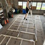 A person standing on a ladder over a floor under construction, smiling at the camera.