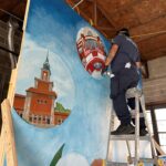 A man on a ladder painting a mural.