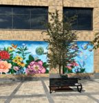 A vibrant mural depicting flowers and celestial elements behind a tree and a park bench.